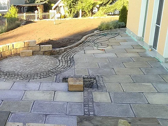 Alte Granitplatten als Terrassenbelag mit Natursteinmauer im Garten