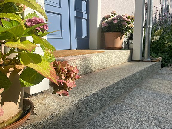 Granitstufe und Granitplatten am Hauseingang mit blauer Haustür und Blumen